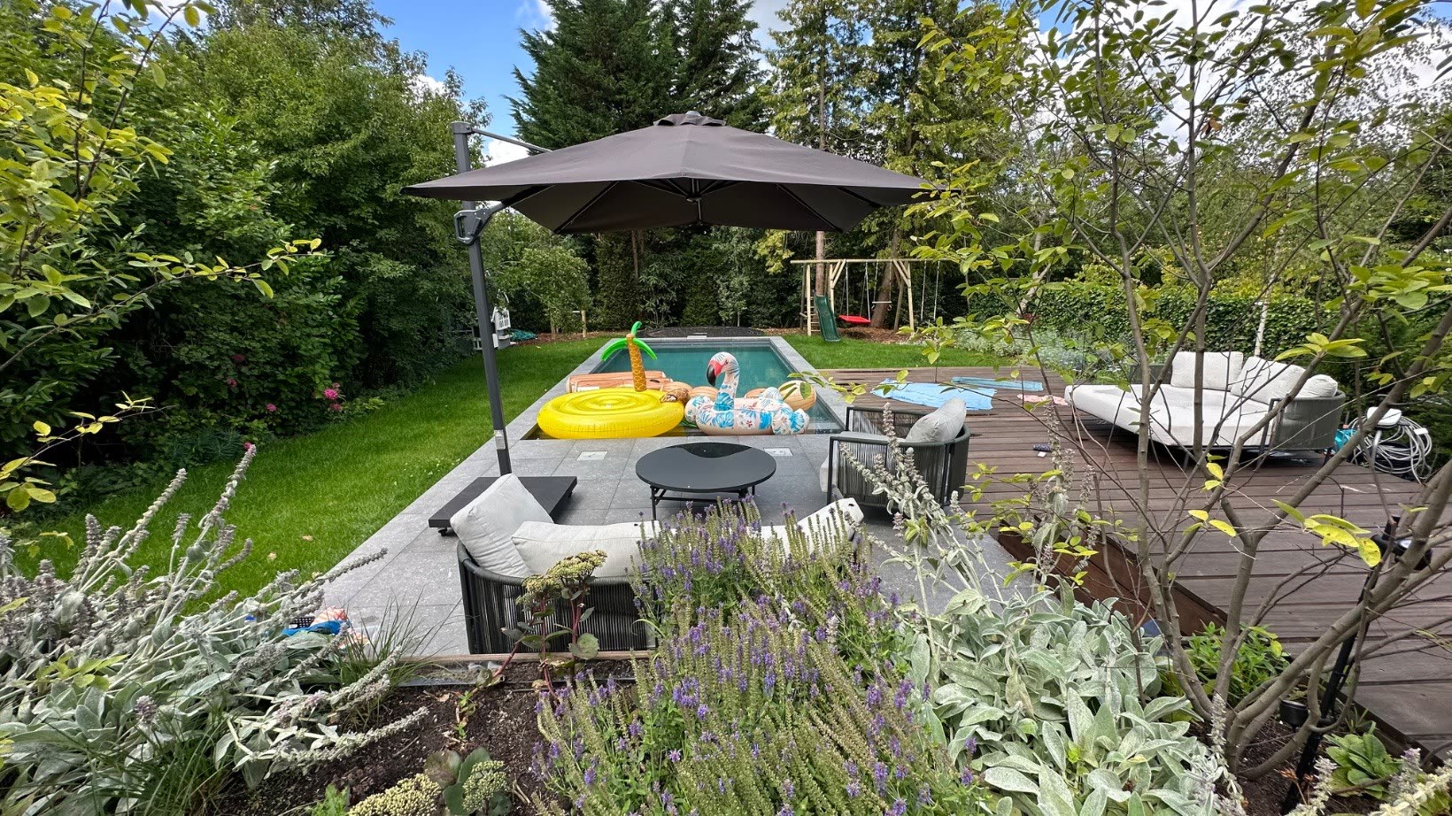 Landscaped planting borders with a parasol beside the pool