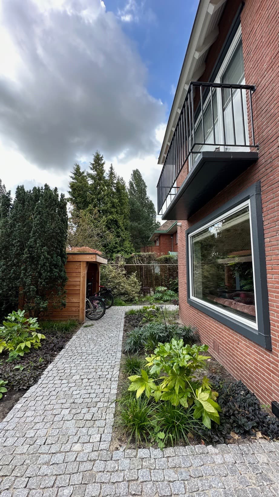 Side path with a covered bike shed, balcony above and side garden