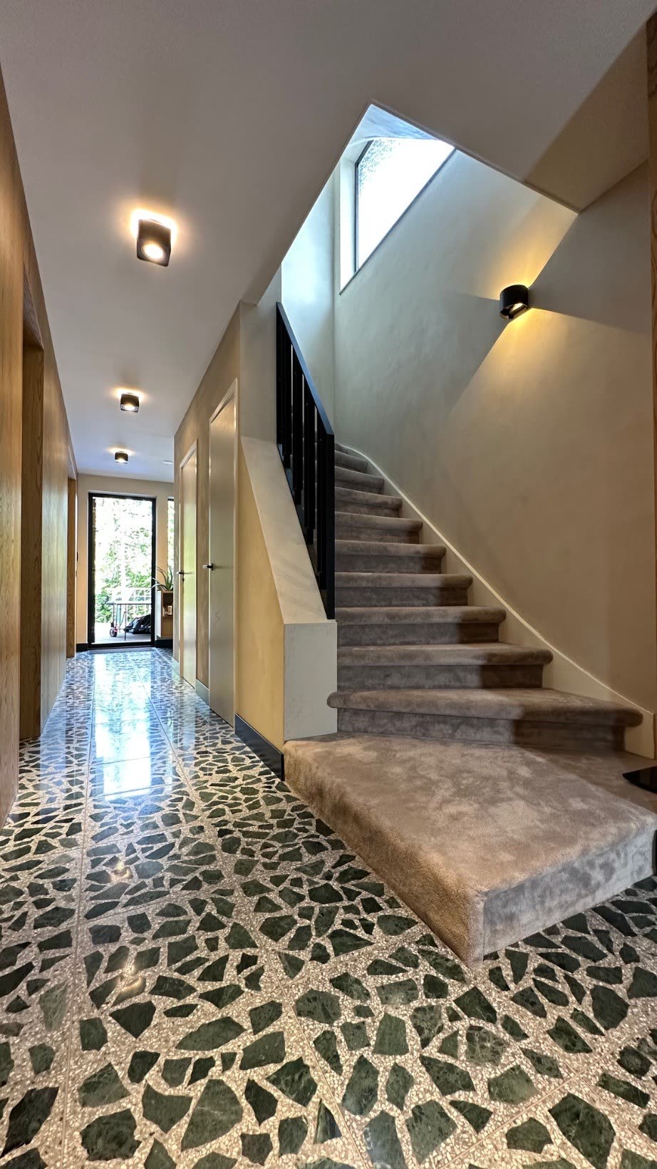 Hallway with green terrazzo floor and the carpeted staircase beneath the stair window